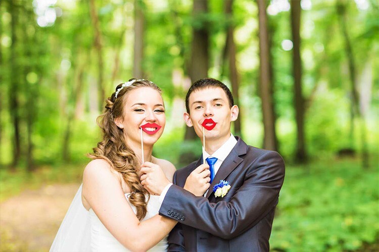 Bride and groom posing with red lip photo booth props in a forest - Snappy Photobooths
